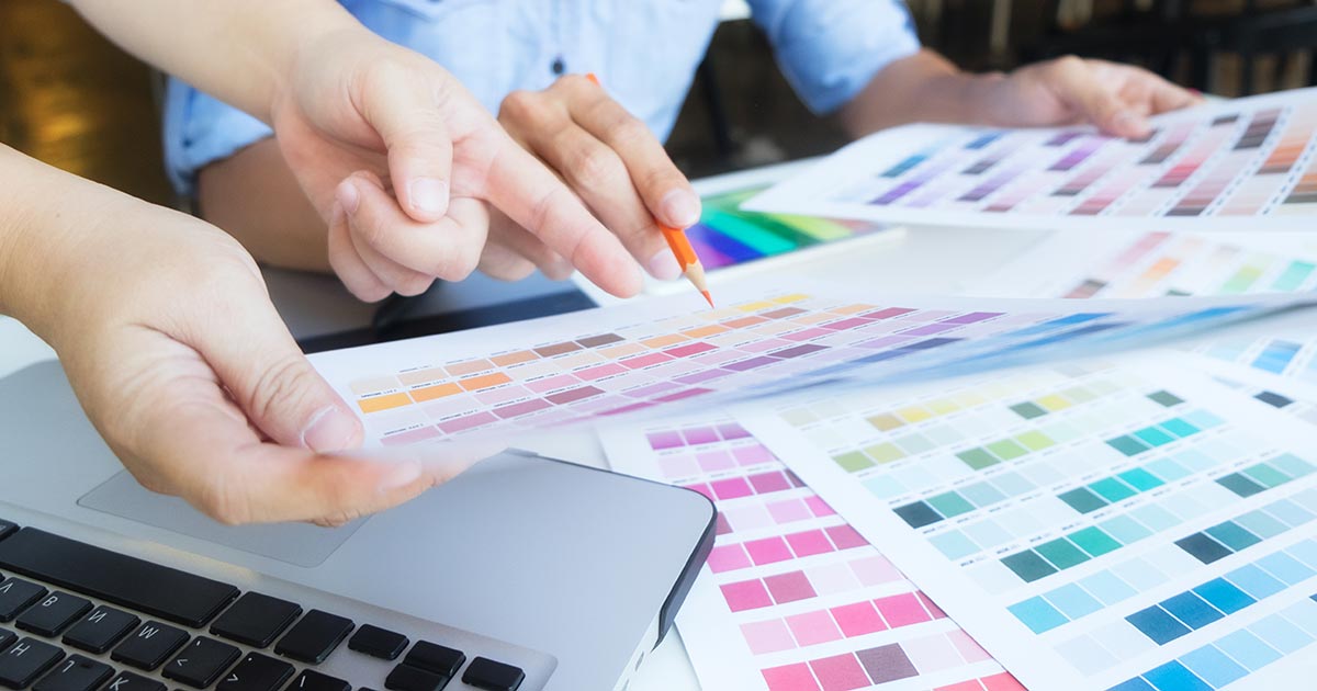 Grafisch ontwerper selecteert kleuren uit kleurenwaaiers en stalen voor logo ontwerp, met laptop en Pantone kleurstalen op tafel